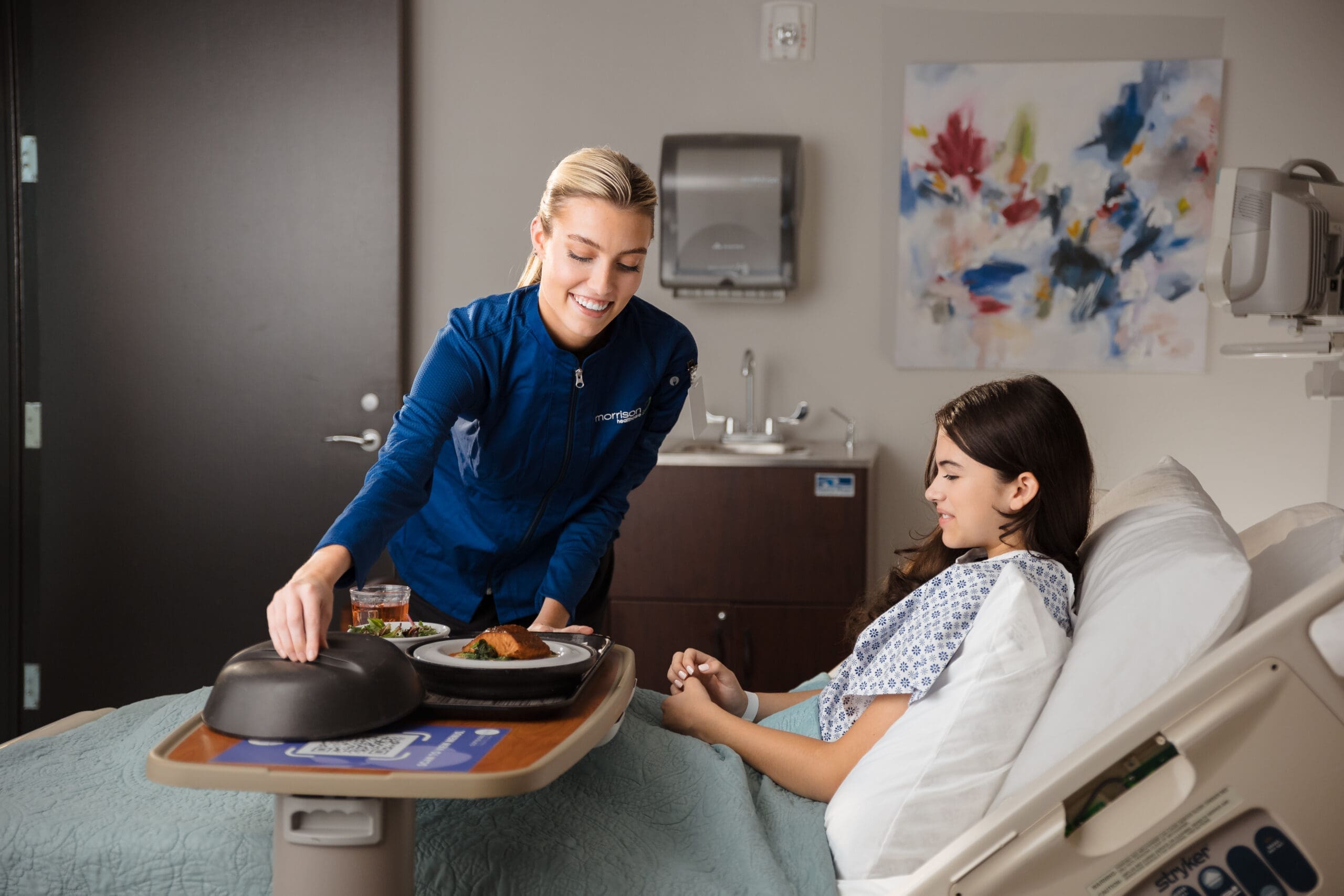 Smiling nurse serving meal to patient in hospital room
